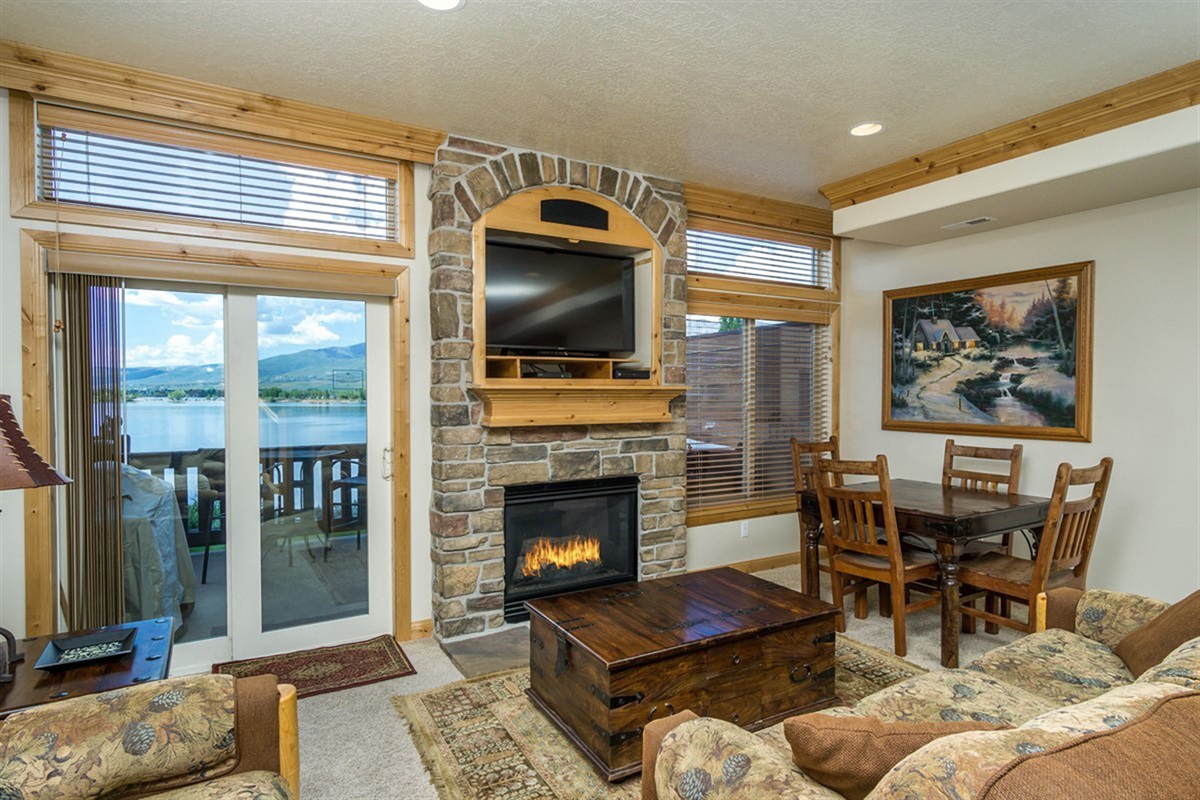 A warm and inviting living space centered around a stone fireplace, with large windows framing stunning lake views and filling the room with natural light.