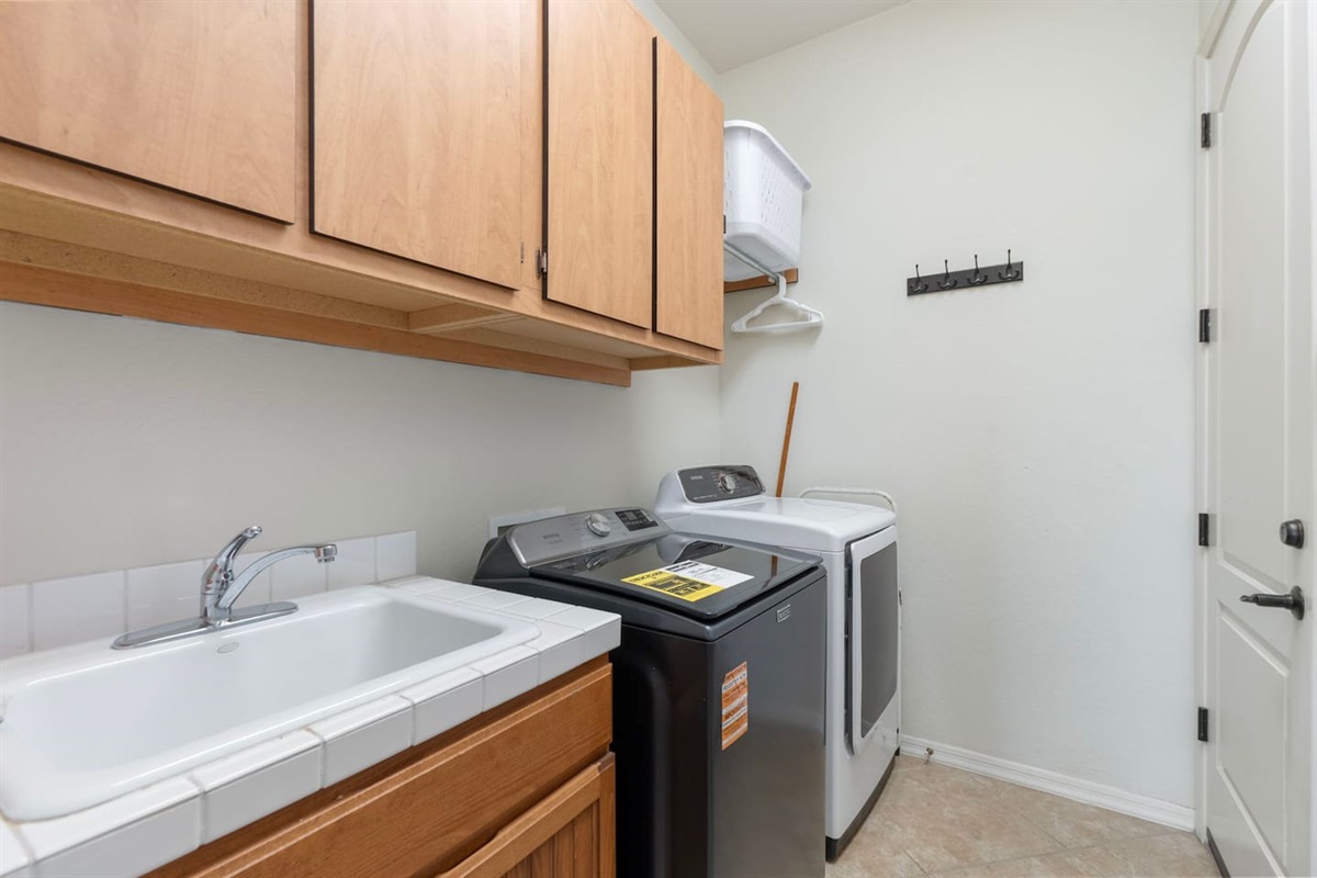 Laundry area with full-size washer and dryer, utility sink, overhead storage cabinets, and wall hooks for added convenience.