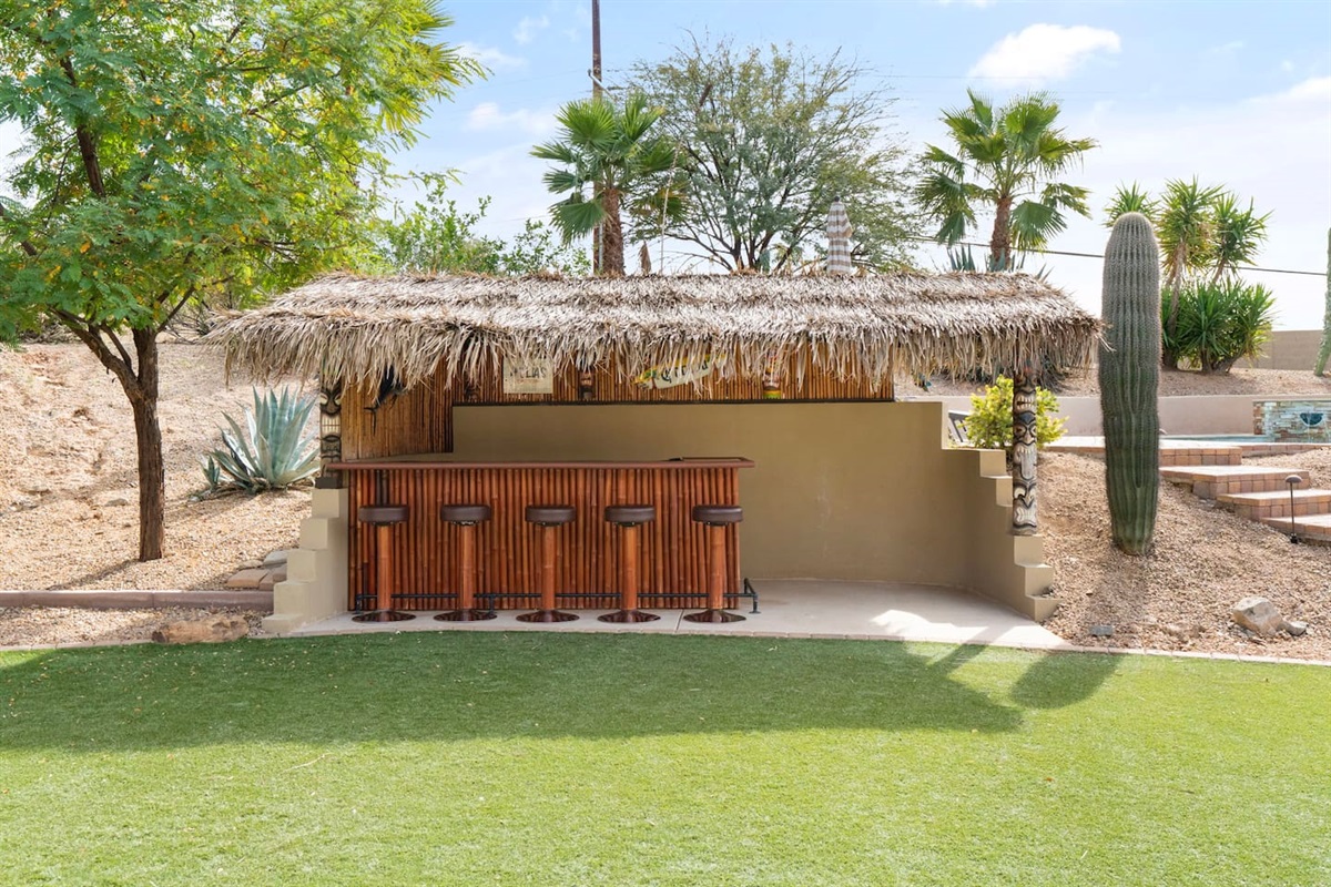 Backyard tiki bar with a thatched roof, bar seating, and a fun tropical vibe—perfect for evening drinks.