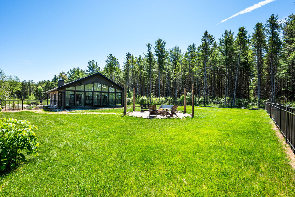 Enjoy the best of the outdoors on the expansive fenced lawn, where the glass-gabled sunroom and stone fire pit sit surrounded by majestic pines.