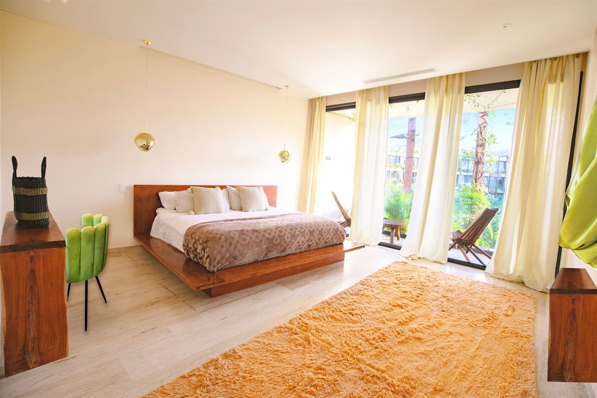 King sized bed in a large room with a desk area, private balcony and local art. 