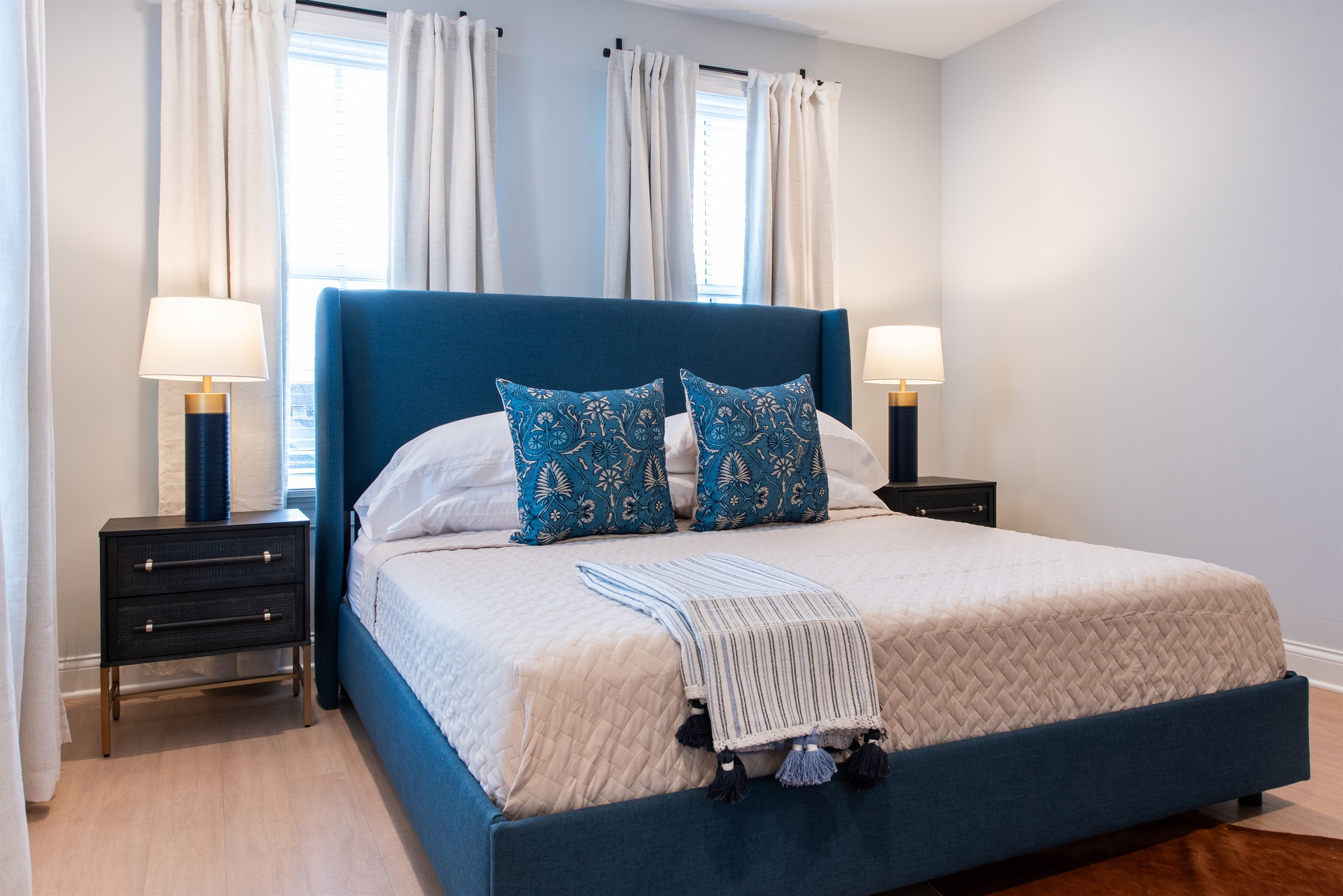 : Experience ultimate relaxation in this beautifully appointed bedroom featuring a plush blue upholstered king bed, elegant decor, and ample natural light. The perfect blend of style and comfort awaits you on the Bourbon Trail.