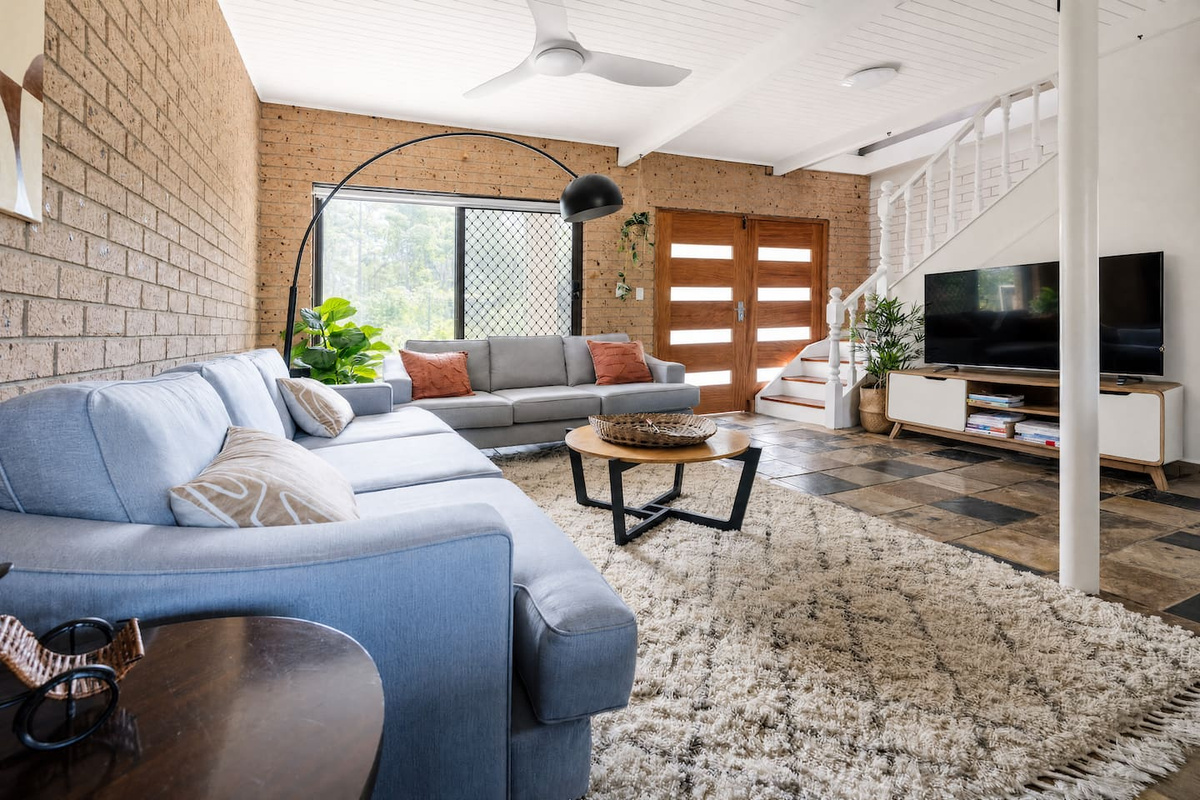 Located near the main entrance, this downstairs living area features two comfortable sofas, a TV, ceiling fans, and a TV unit with books and board games.