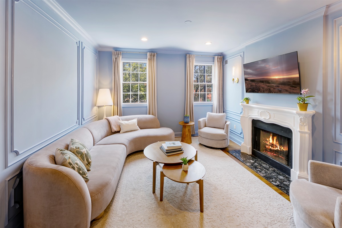 Charming living room featuring a curved sofa, large sun-filled windows, and sophisticated wall detailing