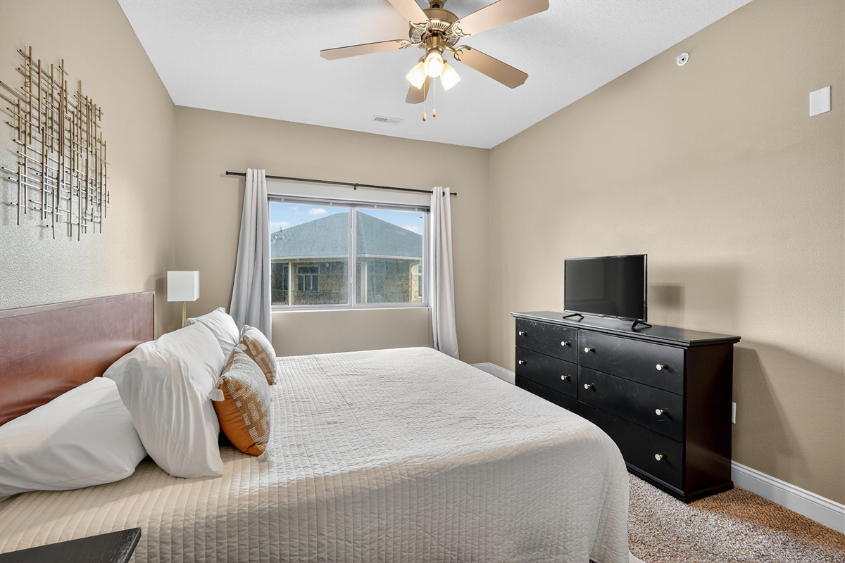 Another view of the calming king suite—neutral tones, plush bedding, and a flat-screen TV at the foot of the bed. A tranquil retreat designed for restful nights and peaceful mornings.