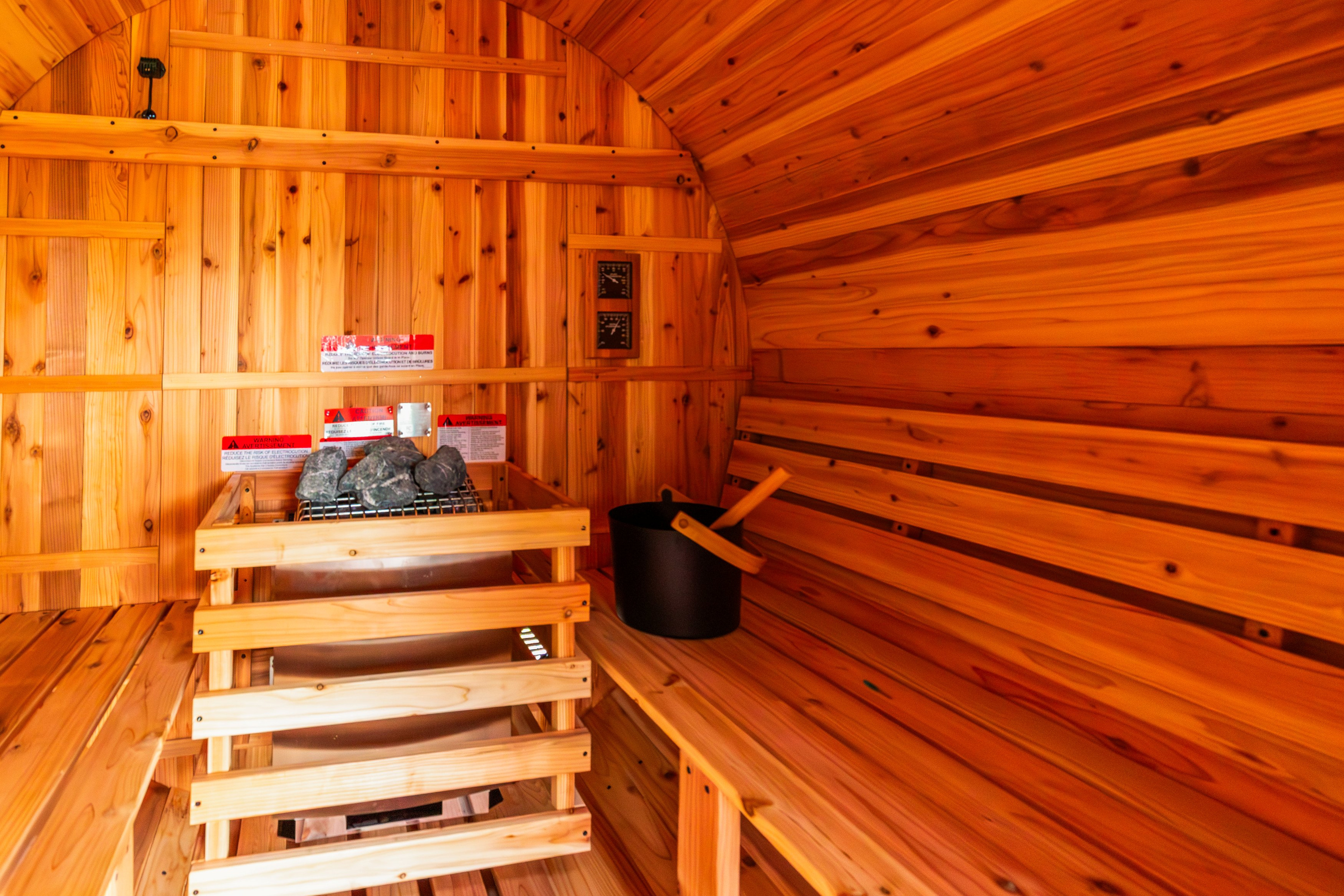 Interior of the private cedar barrel sauna with electric heater, sauna rocks, and bench seating.