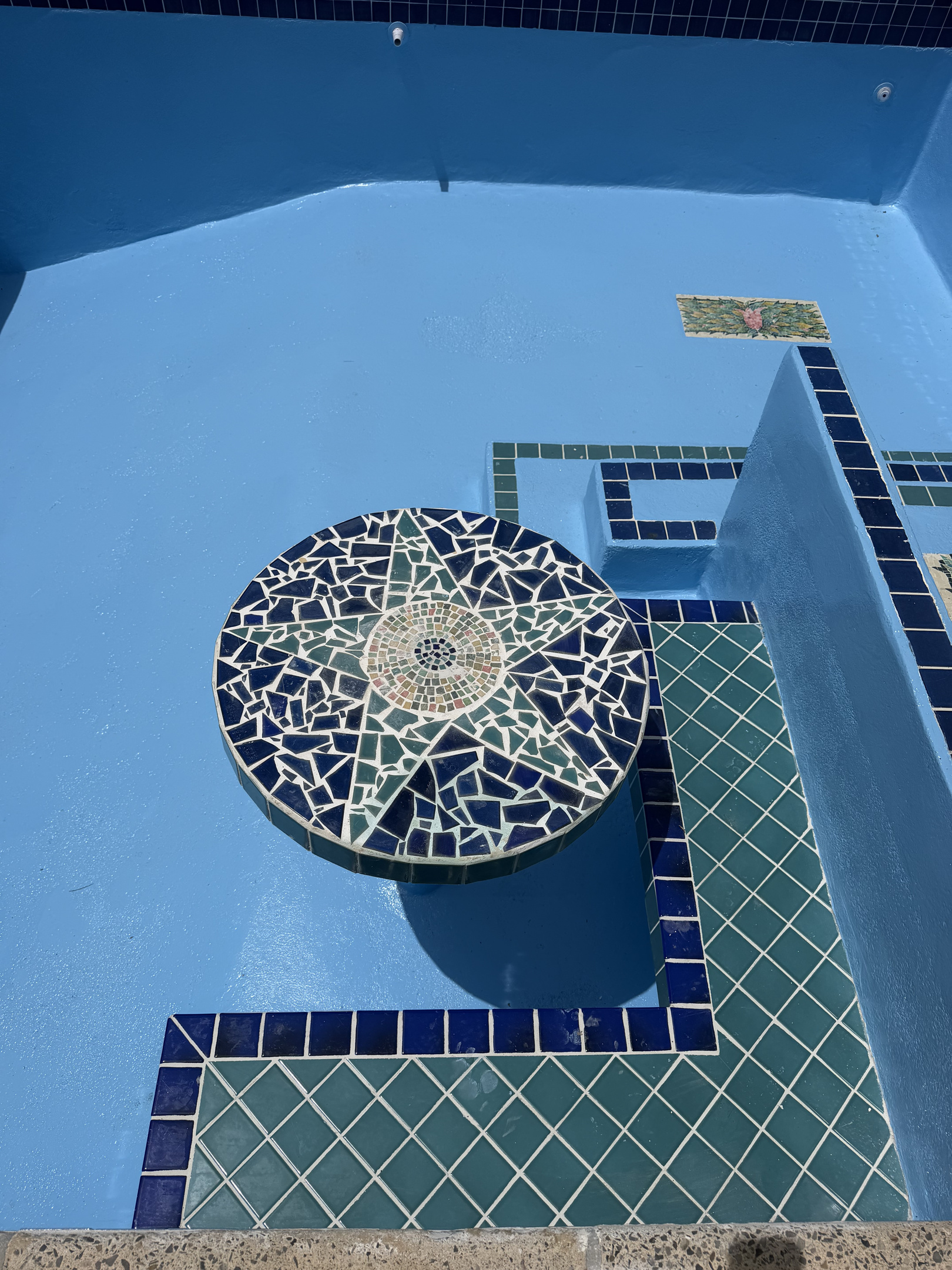 The pool features a unique in-water mosaic table and stepped seating area, perfect for a refreshing dip and conversation.