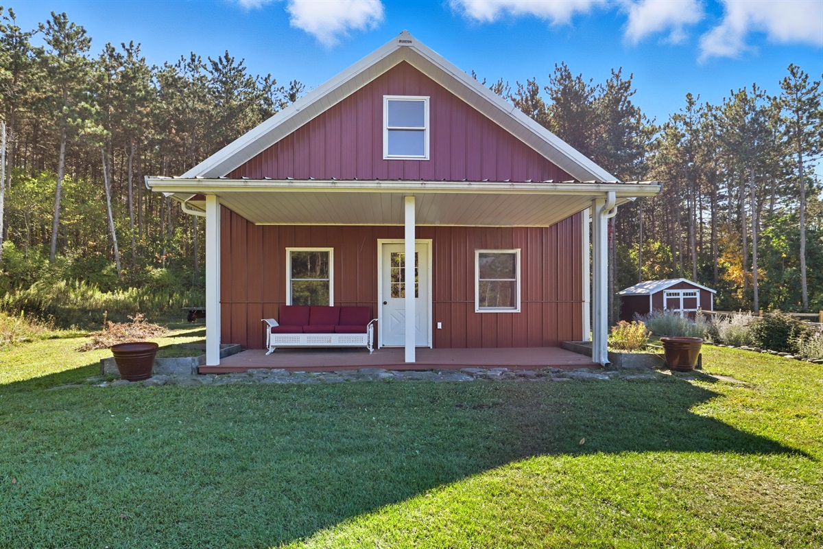 Charming red cabin with a cozy front porch swing, perfect for sipping coffee while enjoying peaceful countryside views.