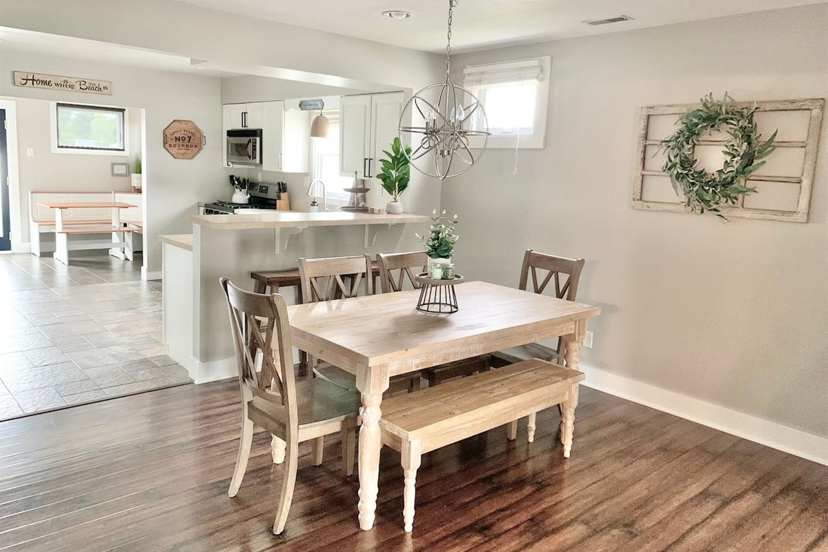 This inviting dining area features a rustic farmhouse table with bench seating and a striking orbital chandelier. The open layout provides a clear view of the kitchen and breakfast nook, making it easy to enjoy meals together during your stay.