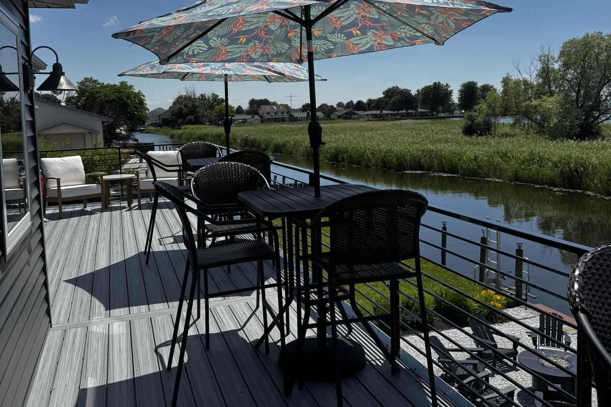 Outdoor deck dining area overlooking a peaceful canal, featuring patio seating under a patterned umbrella—perfect for relaxing, dining, and enjoying waterfront views.