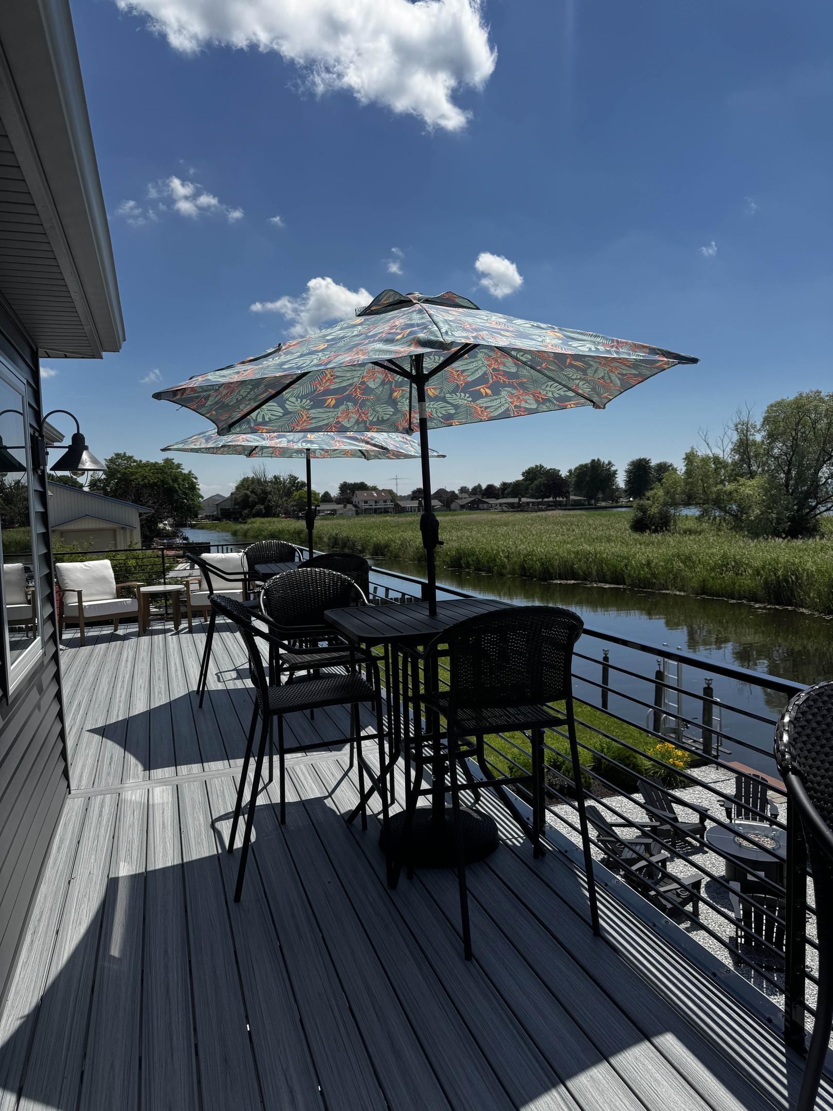 Outdoor deck dining area overlooking a peaceful canal, featuring patio seating under a patterned umbrella—perfect for relaxing, dining, and enjoying waterfront views.