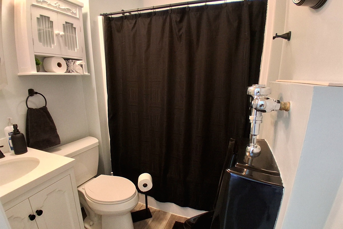 Designed for refined taste, this men’s bathroom features a sleek wall-mounted urinal, a mirrored Kohler medicine cabinet, and over-the-toilet storage. Black accents add bold contrast and modern polish to this calm, carefully curated space.