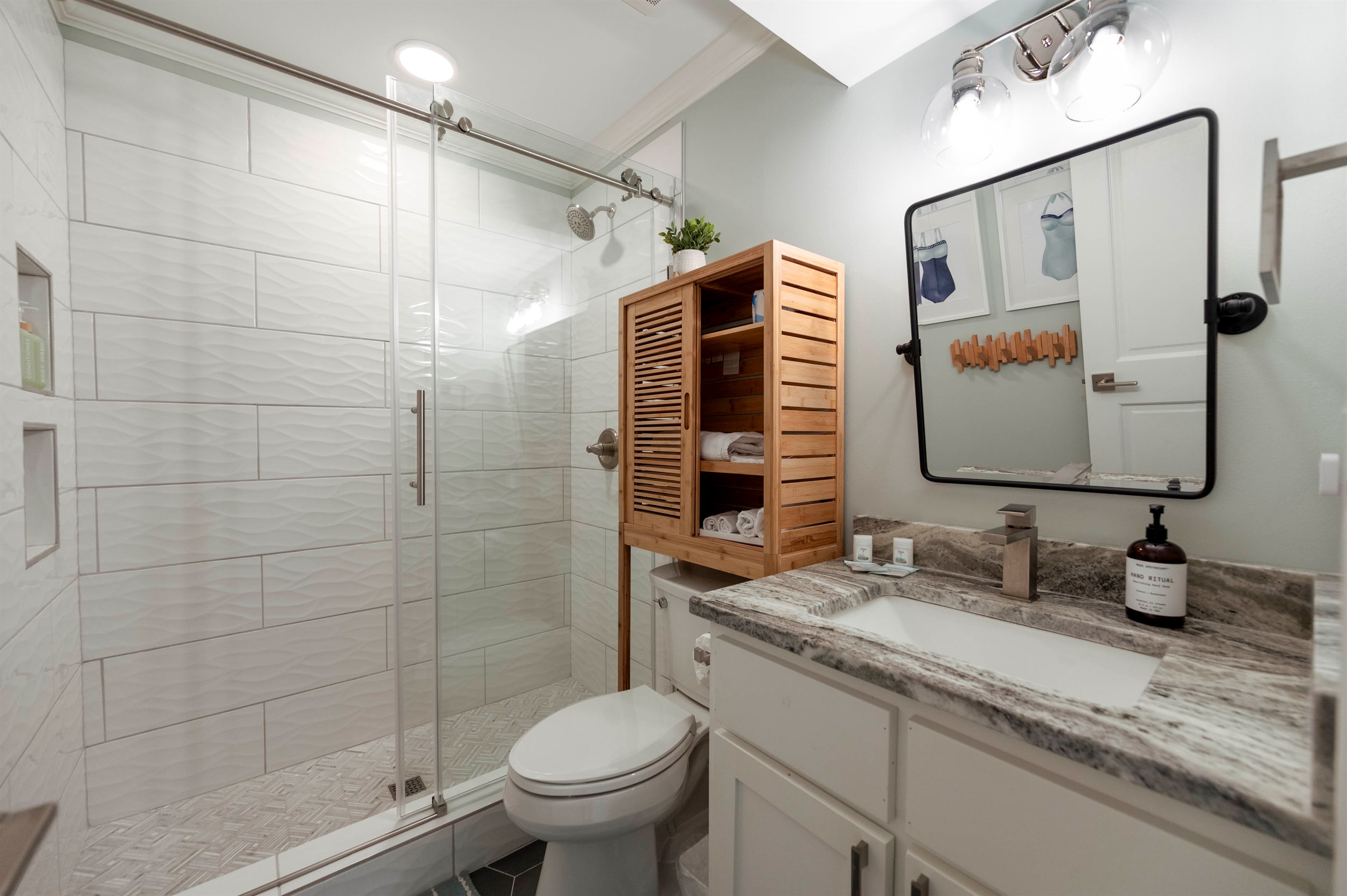 Bright modern bathroom with a glass shower, marble countertop, cozy wooden accents, and sleek fixtures.
