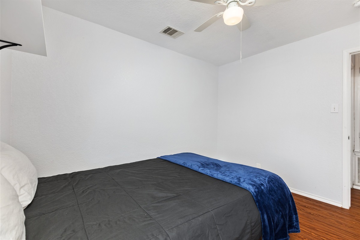 Queen bedroom with ceiling fan, plush navy bedding, natural light, and hardwood floors. Extra pillows and blankets provided. Current decorative blankets, bedding, and wall art are not shown in these photos.