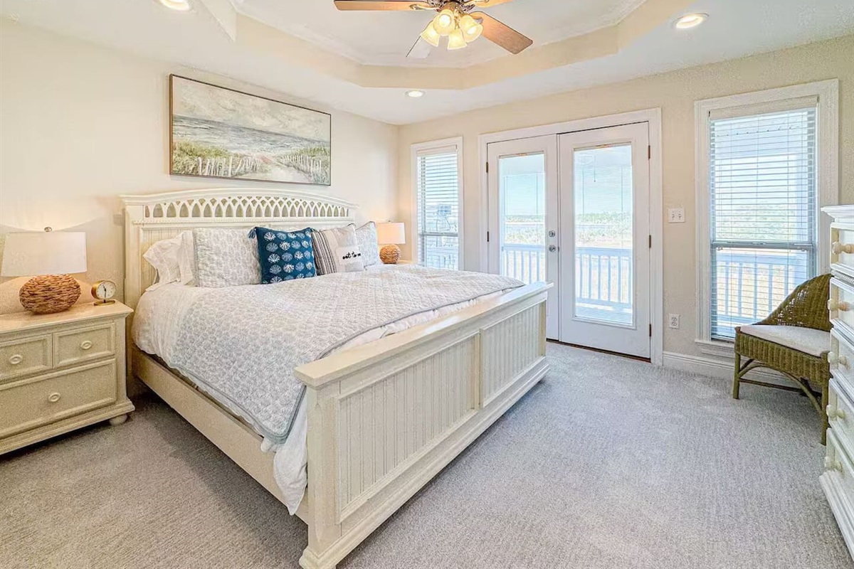 Relaxing primary bedroom with a plush king bed, soft coastal decor, and warm lighting. Includes bedside lamps, ceiling fan, and a peaceful, resort-style feel.