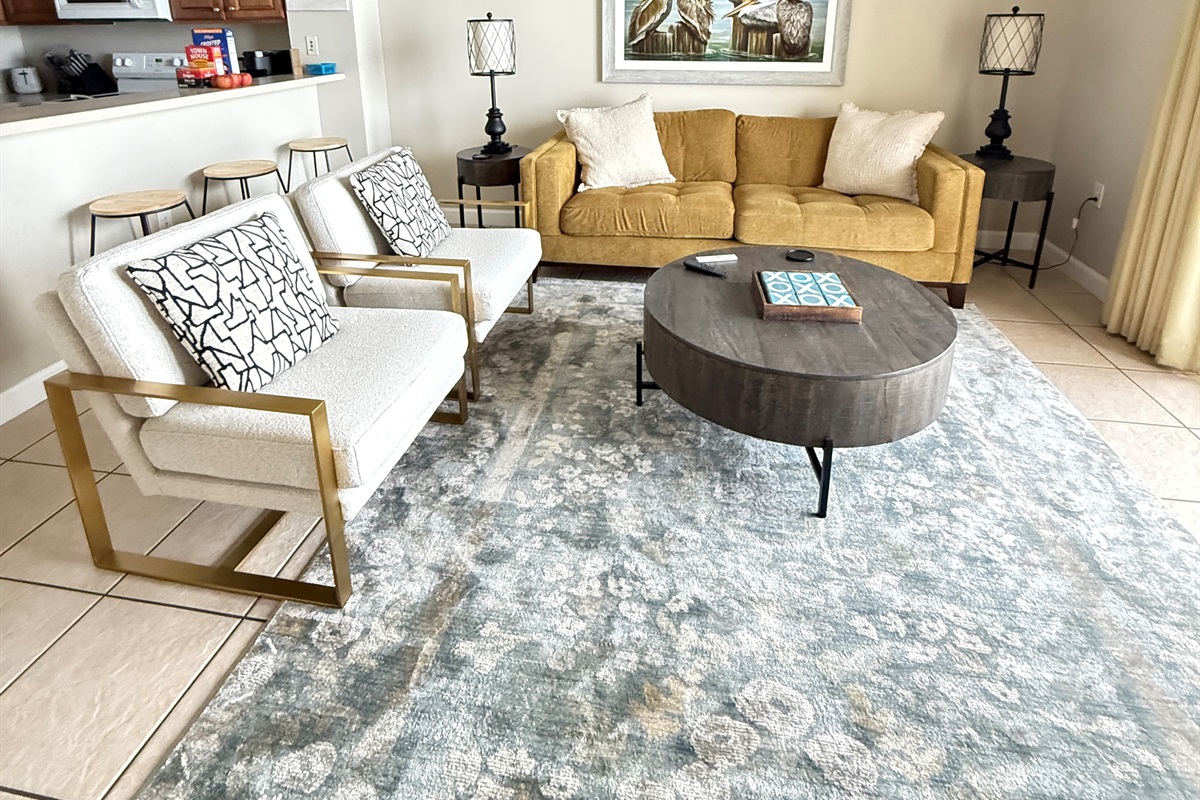 Unwind in this bright, stylish living space designed for comfort after a perfect beach day. The cozy sofa, modern chairs, and soft coastal tones create the perfect spot to relax, watch a movie, or gather with family and friends. Just steps away from the ki