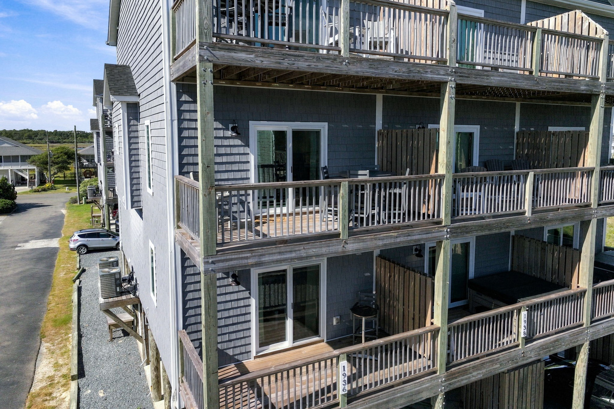 Close-up aerial view highlighting the multi-story exterior balconies with wooden railings, privacy dividers, outdoor seating options, and sliding glass doors.   