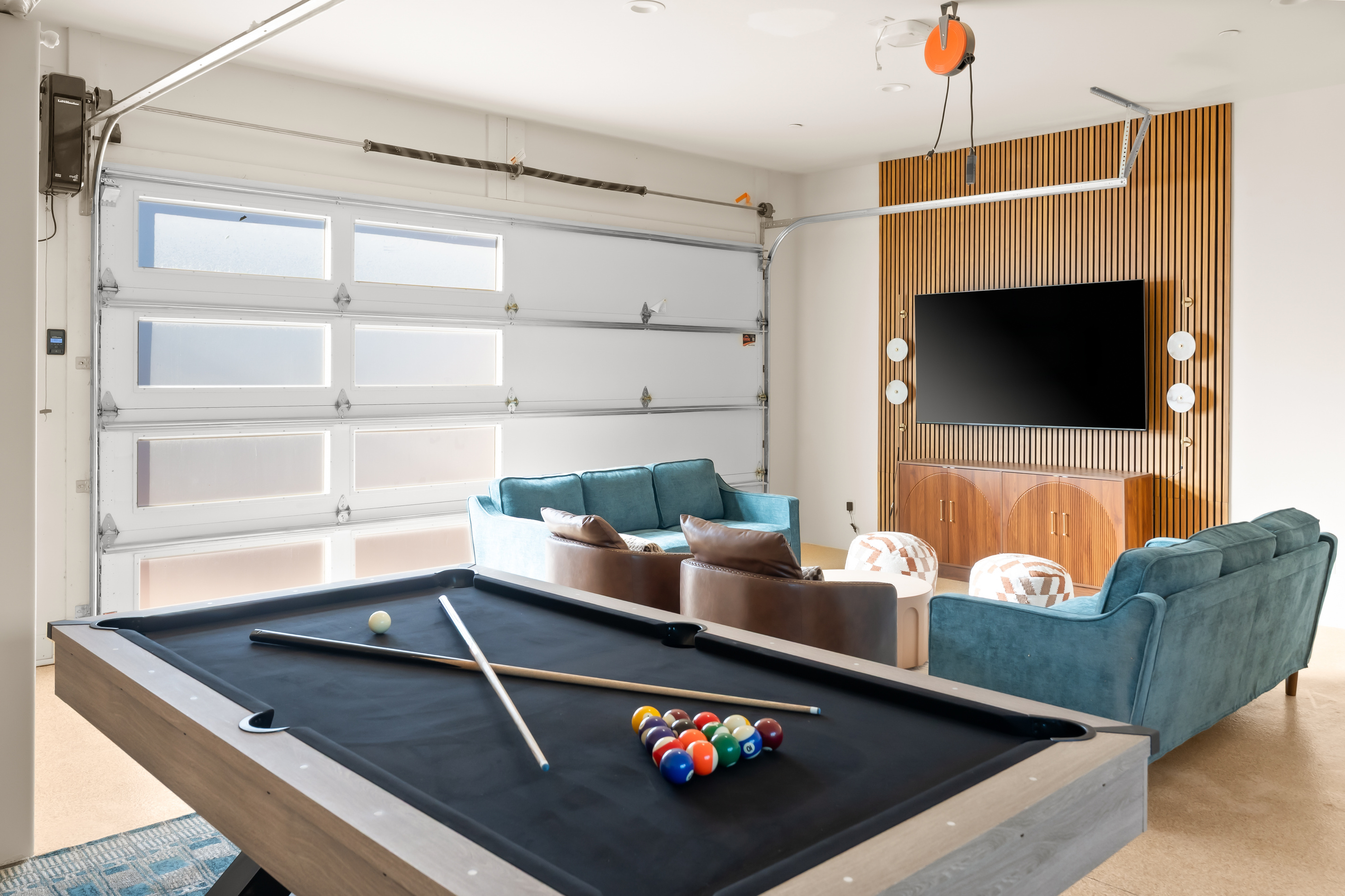 Ultimate game room lounge with a sleek black felt pool table, massive 75" smart TV, wood slat media wall, and plush seating for game day.