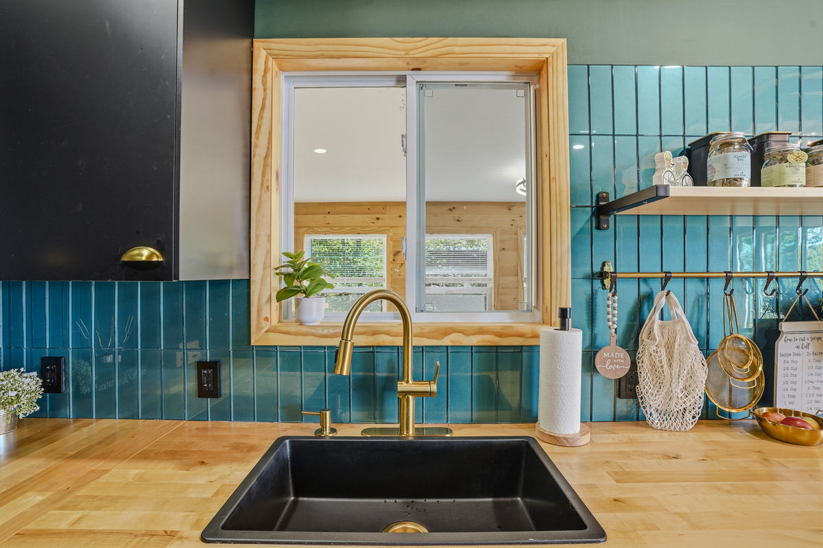 Chef's kitchen with black undermount sink, brass faucet, and teal tile backsplash