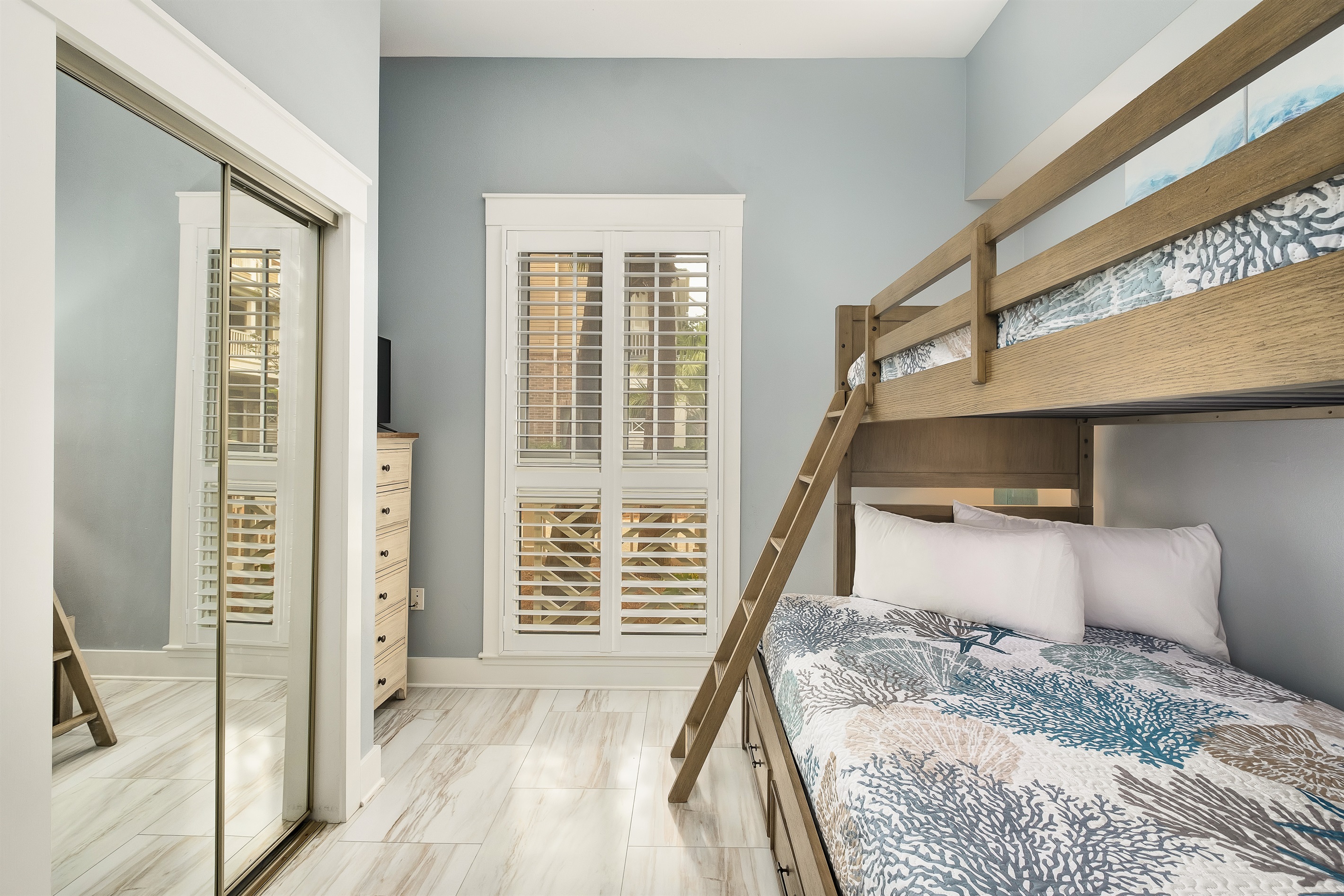 This cozy bedroom features a bunk bed with comfortable bedding. The mirror doors and large windows make the room feel open and bright.