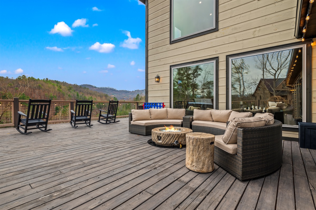 A spacious deck with a cozy fire table conversation area and rocking chairs, perfect for relaxing while taking in breathtaking Smoky Mountain views.