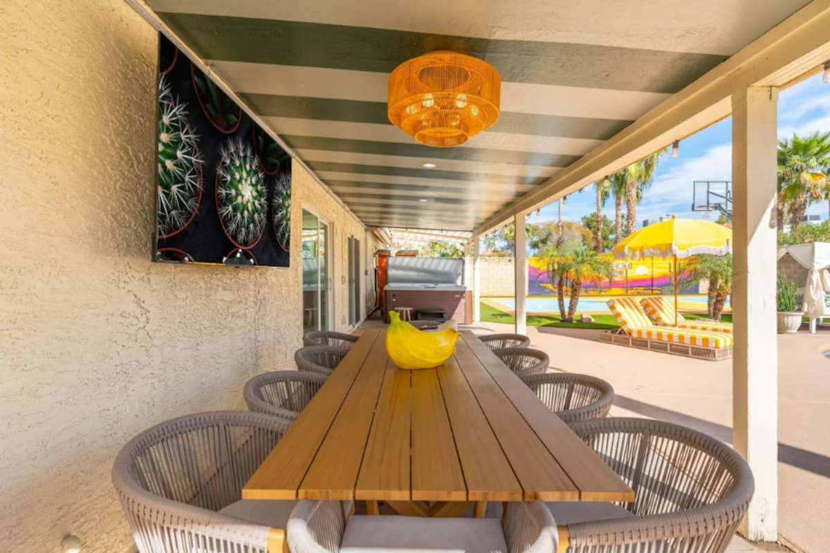 Covered outdoor dining with striped ceiling, long wooden table, and pool views—perfect for al fresco meals and entertaining.