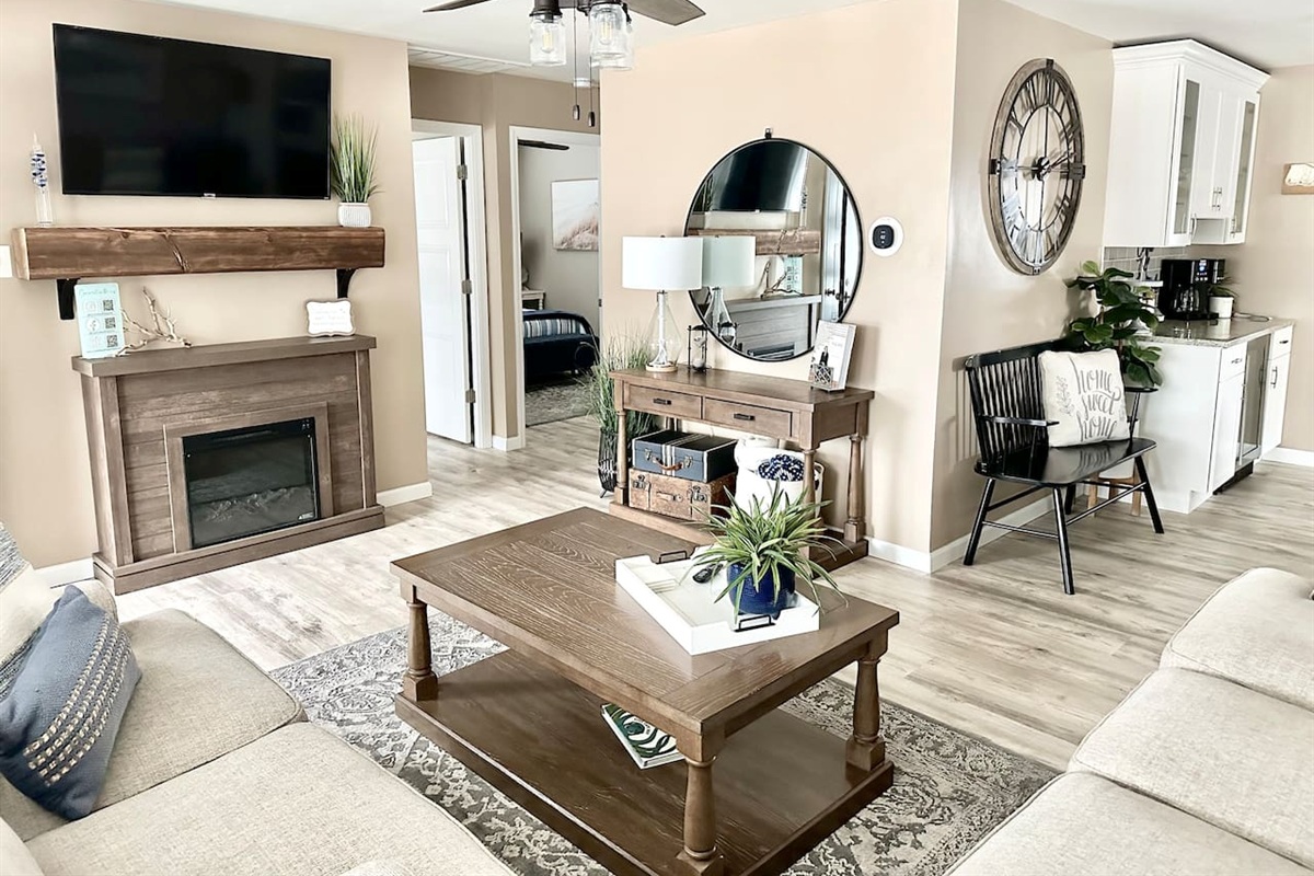 Gather around the warm electric fireplace in our inviting living room. This space features a large flat-screen TV, stylish coffee bar area, and comfortable seating—perfect for cozy evenings in after a long day at the beach.