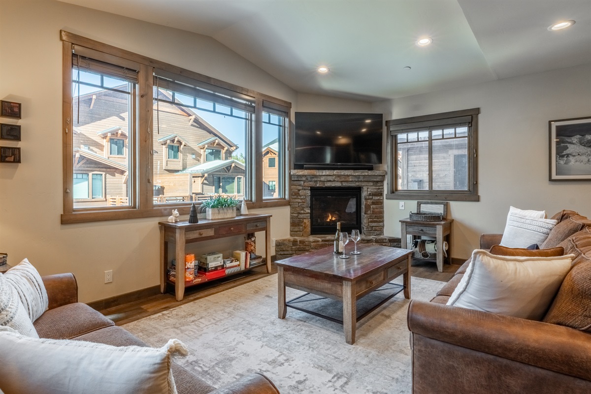 Mountain light pours through expansive windows, framing a warm fireside living space with oversized seating and room for everyone to gather.