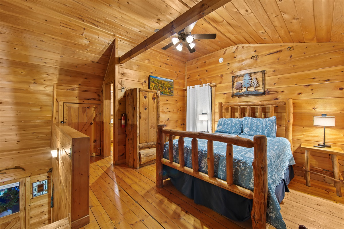 This cabin bedroom exudes charm with its log furniture, cozy blue bedding, and warm wooden walls, offering a relaxing ambiance with natural tones and scenic outdoor access.