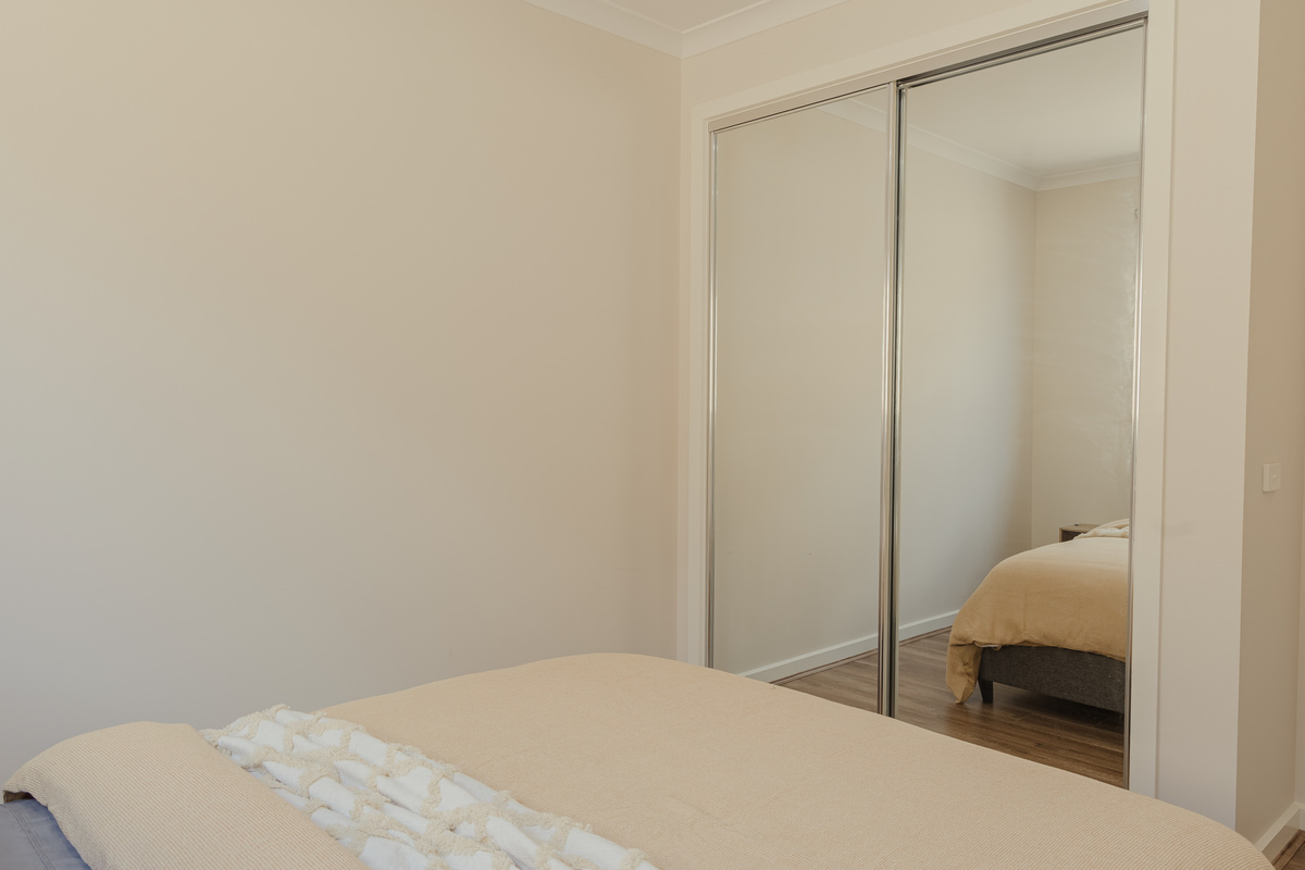 Bedroom3 with queen bed, bedside table, window and neutral styling.
