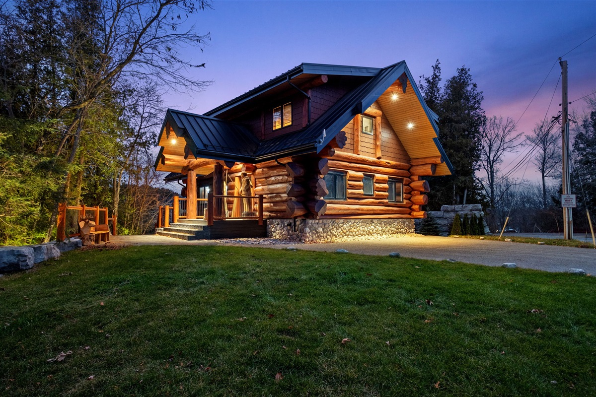 Stunning log home at twilight — handcrafted timber exterior, warm ambient lighting, and a spacious wrap-around porch welcoming you to Bear Lodge.