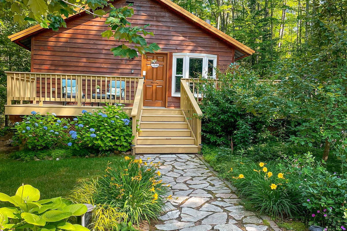 Cottage front and entrance- two lounge chairs in front with foot rests on the 1k wrap around deck. 