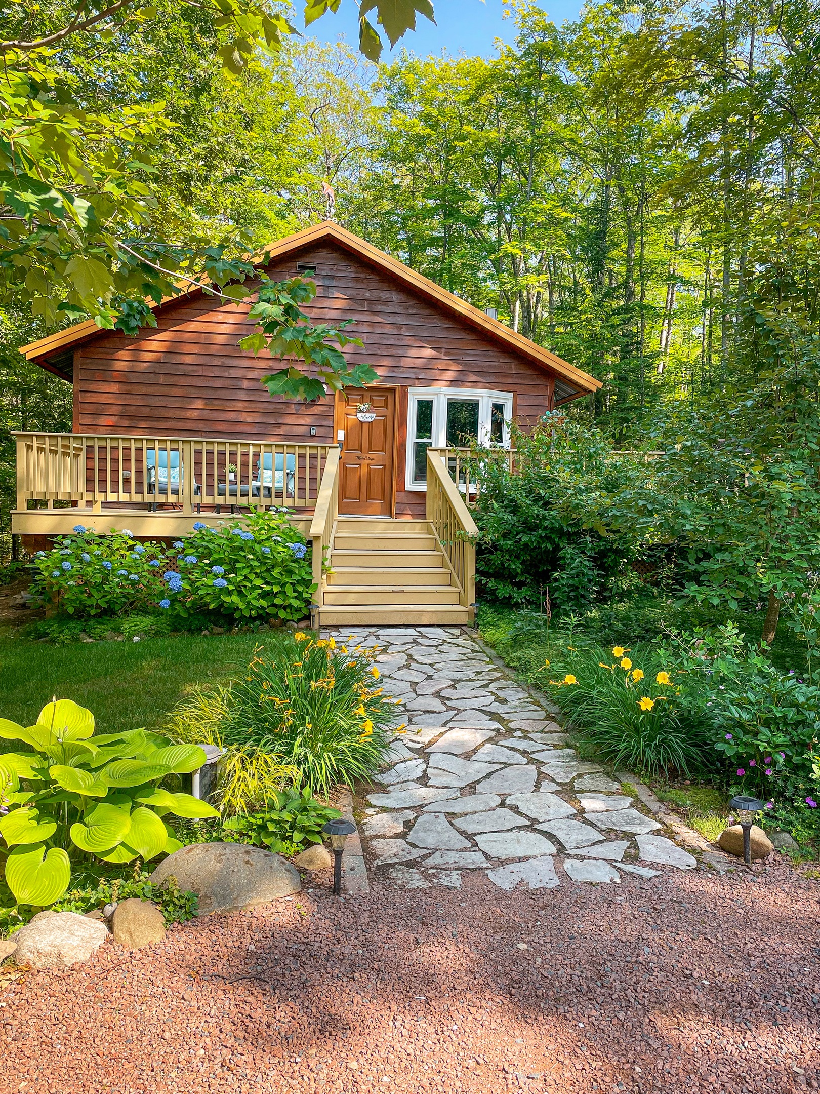 Cottage front and entrance- two lounge chairs in front with foot rests on the 1k wrap around deck. 