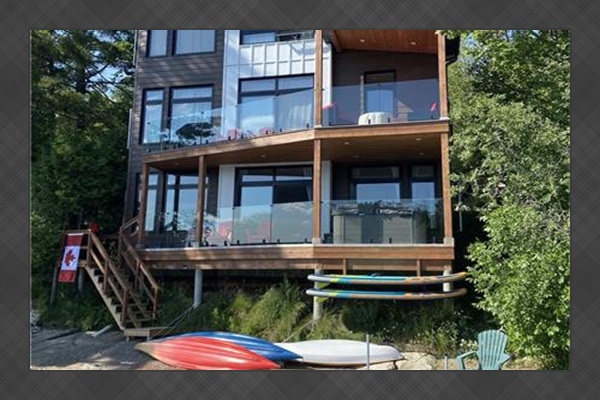 View of cottage from dock showing beach and watercraft; hottub on 1st balcony of cottage.