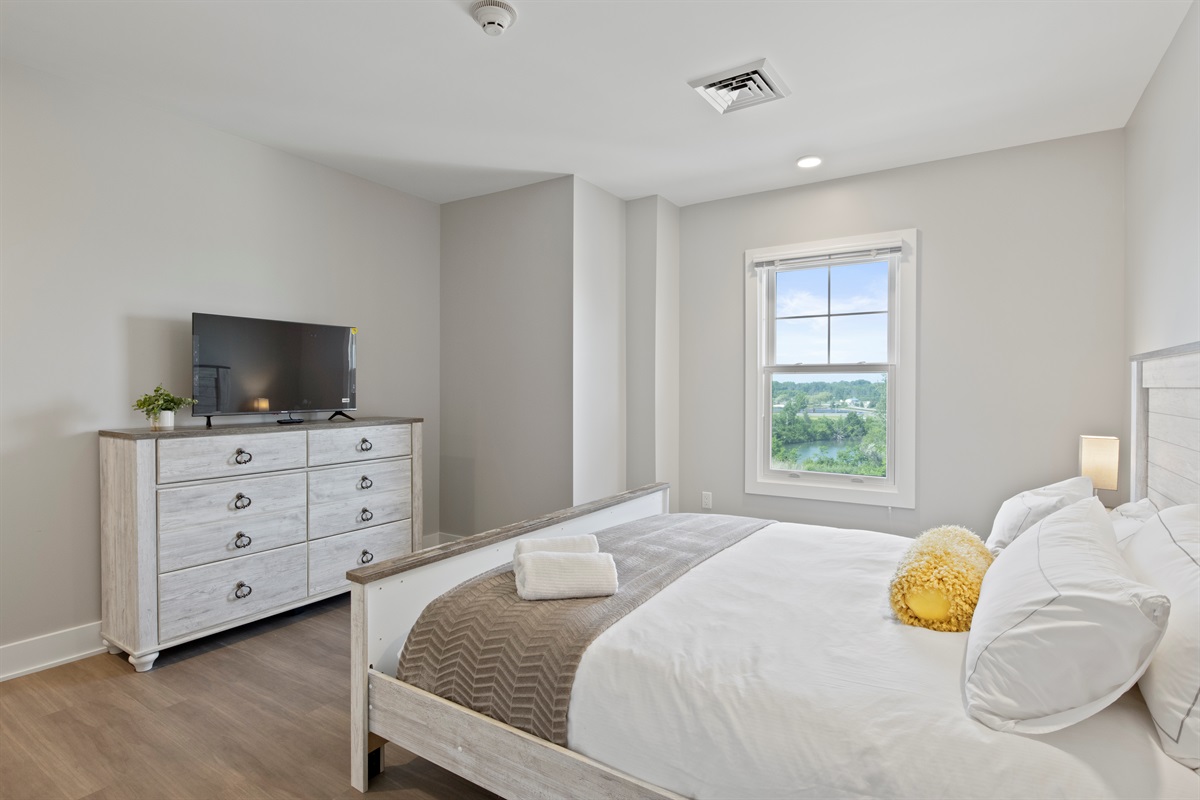 Relax in this bright and spacious bedroom featuring a cozy queen bed, modern lighting, and a serene lake-view window—perfect for your Finger Lakes getaway.