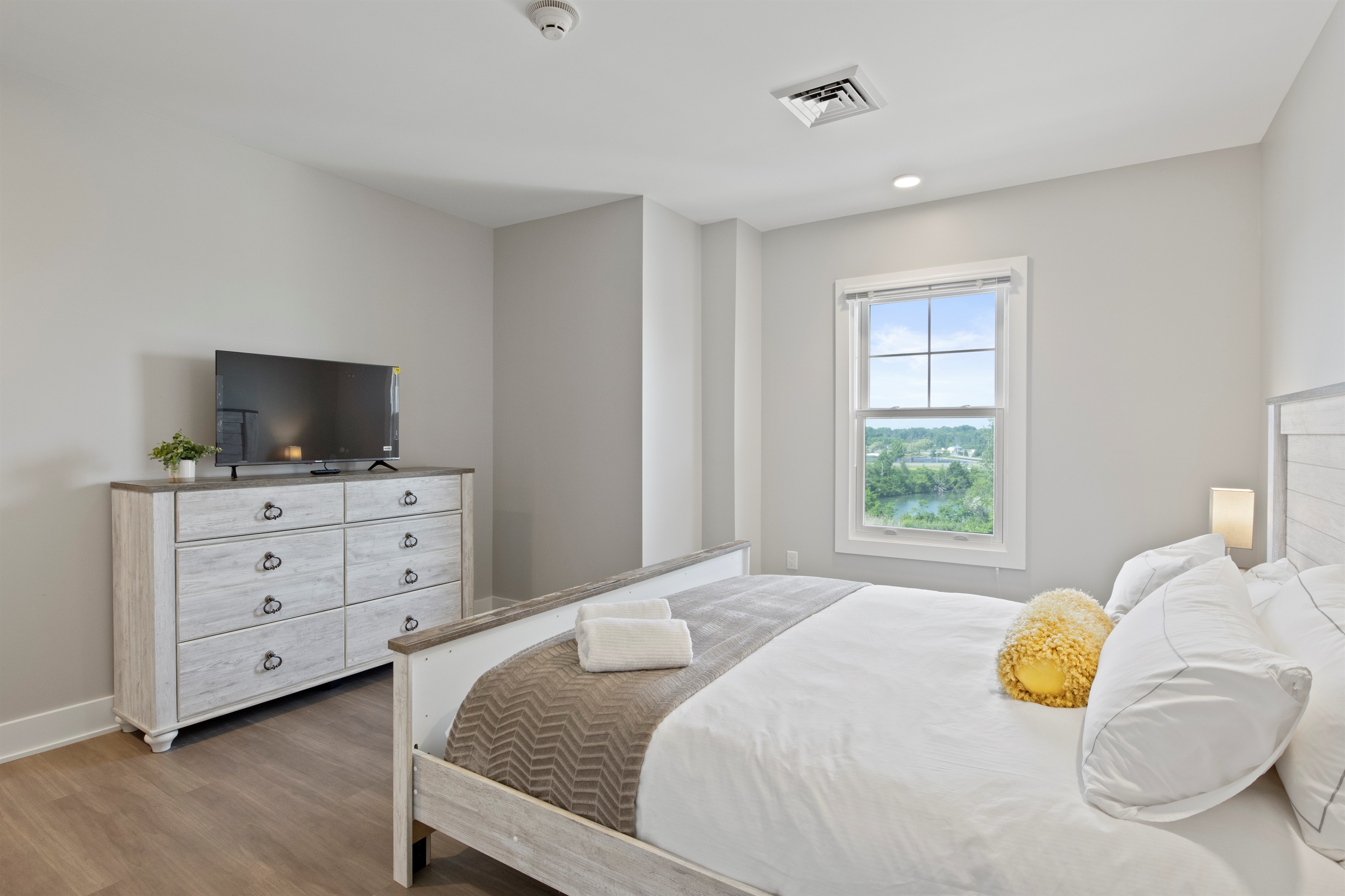 Relax in this bright and spacious bedroom featuring a cozy queen bed, modern lighting, and a serene lake-view window—perfect for your Finger Lakes getaway.