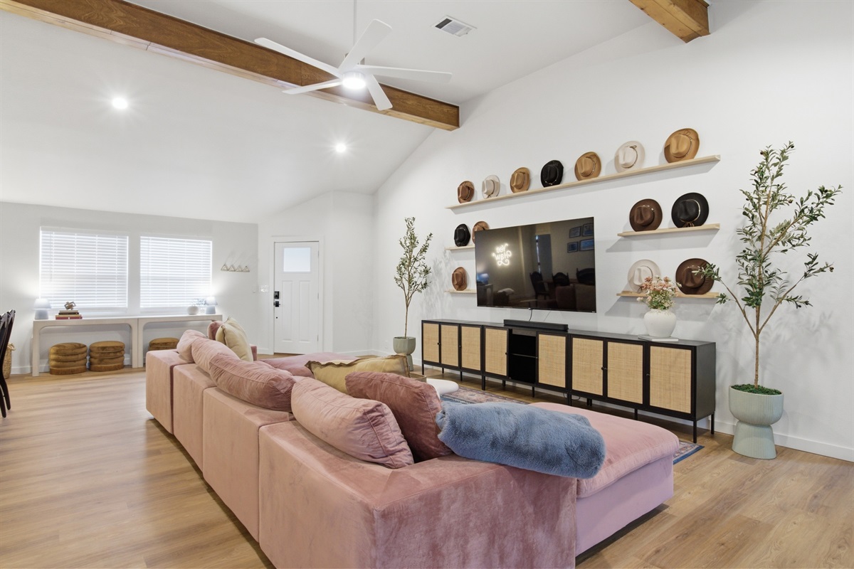 Full living room layout from rear angle showing 75" Smart TV, sectional, and ceiling fan. Spacious common area with Portable Fans available for every stay.