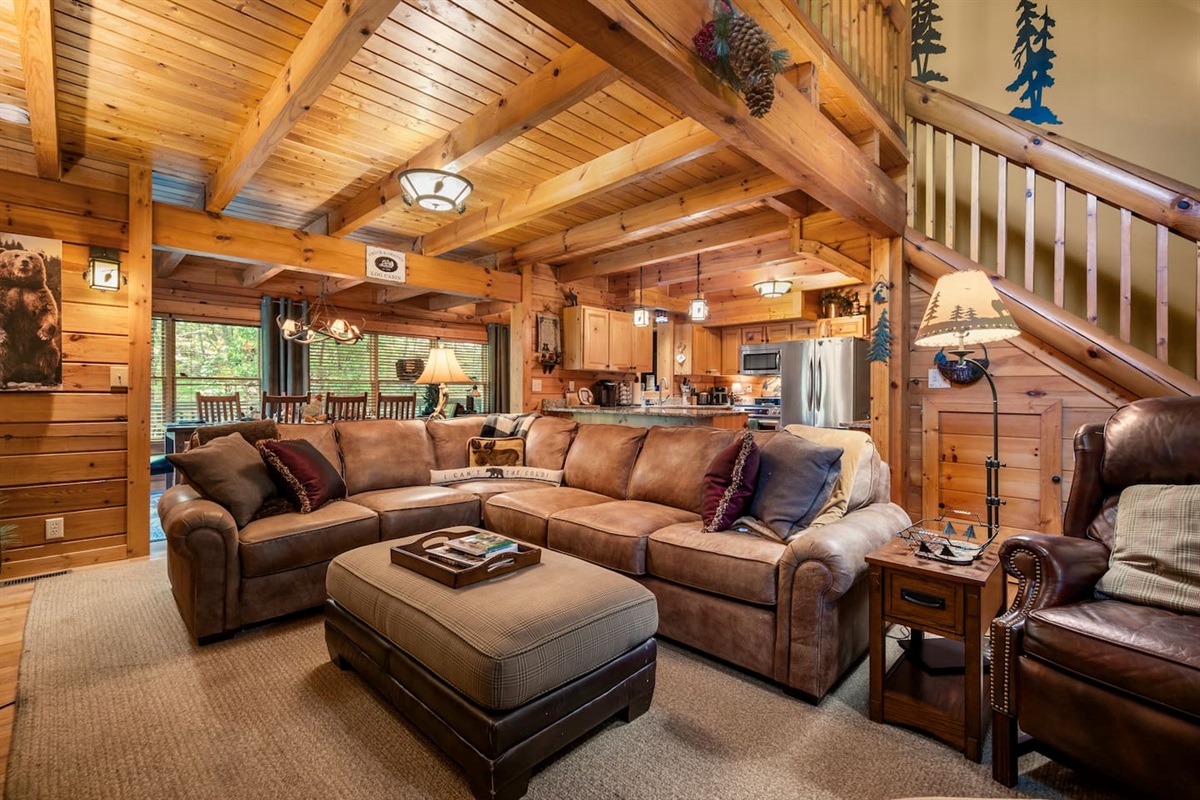 The open-concept main level features a living room with a spacious sectional and additional seating, an overlooking loft, and floor-to-ceiling wood interiors.