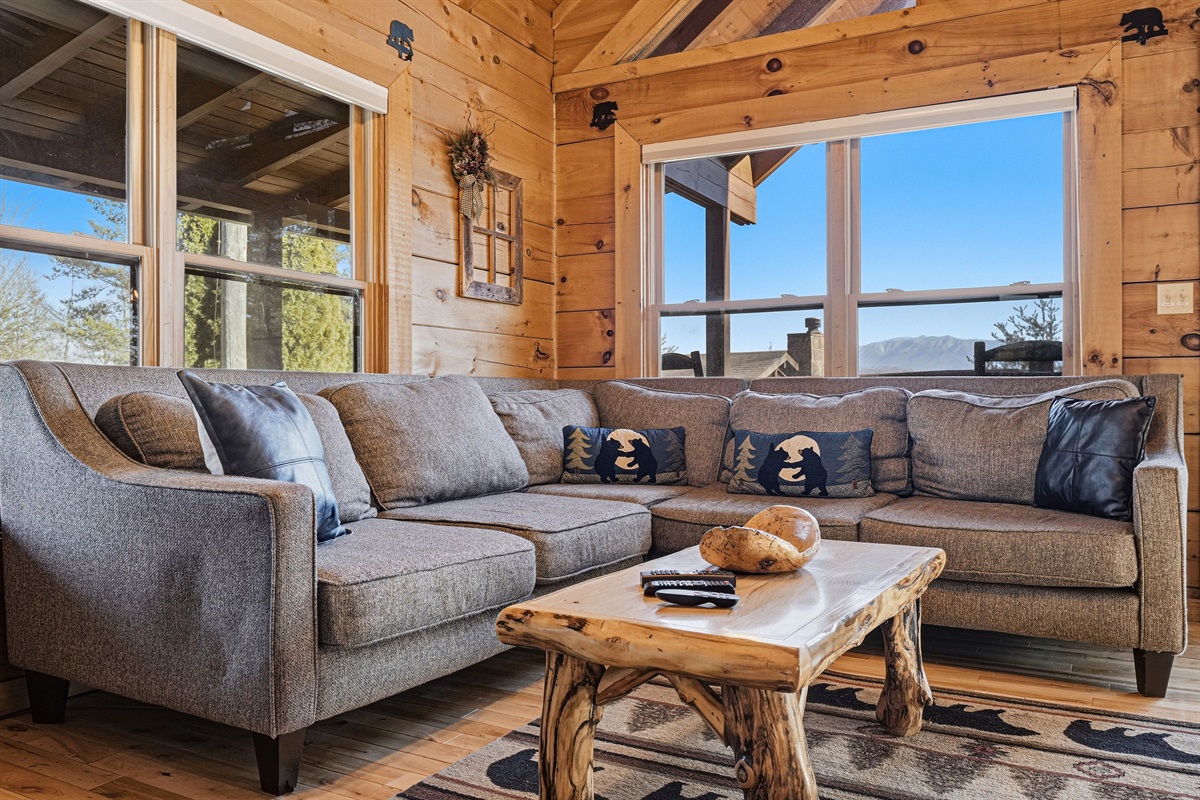 Sink into this oversized sectional and take in sweeping Smoky Mountain ridge views without ever leaving the couch | This Gatlinburg-area cabin rental blends rustic charm with modern comfort &mdash; handcrafted log coffee table, bear accent pillows & floor-to-cei