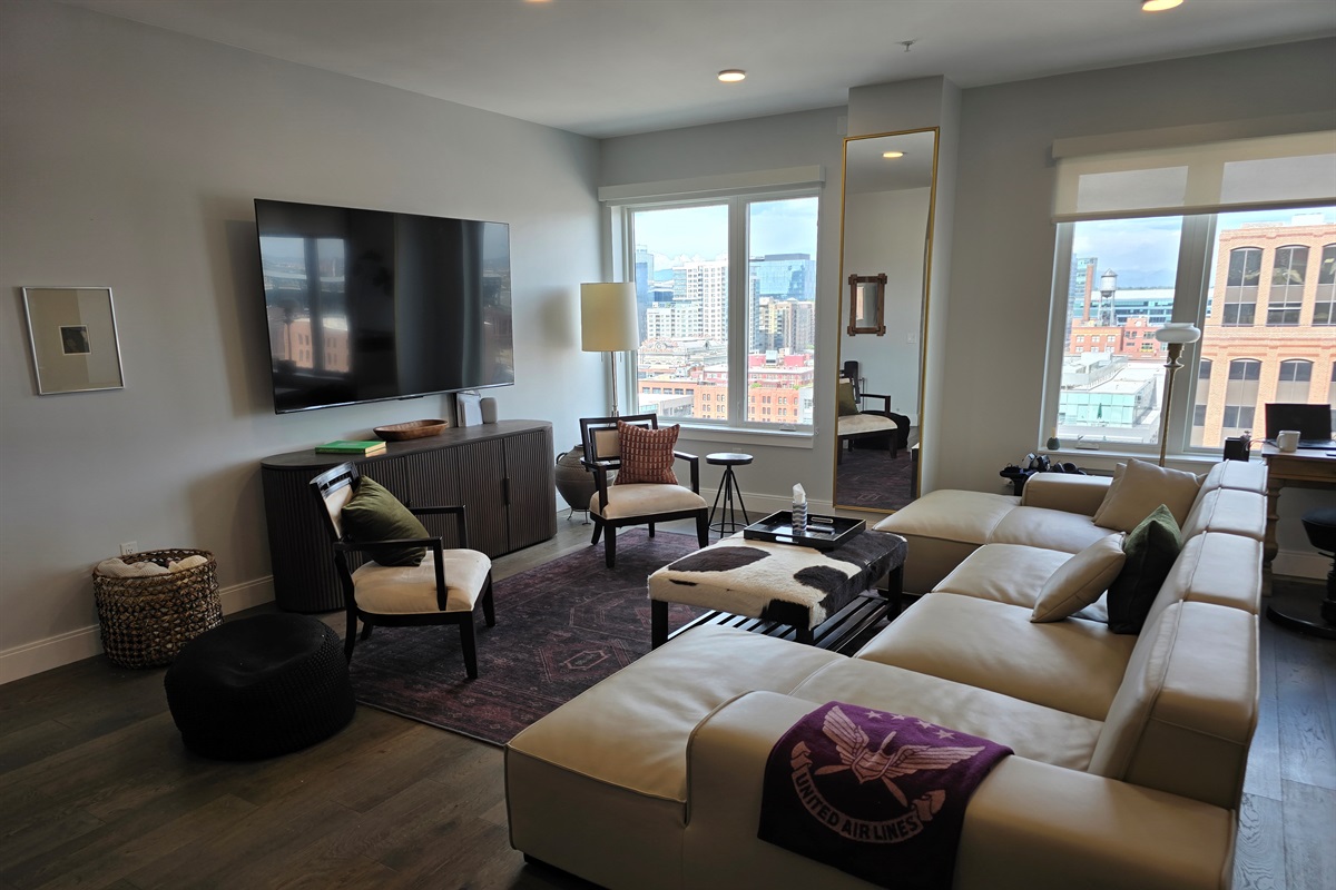 ✨ Spacious living room with designer sectional, 85" Smart TV, and skyline views.