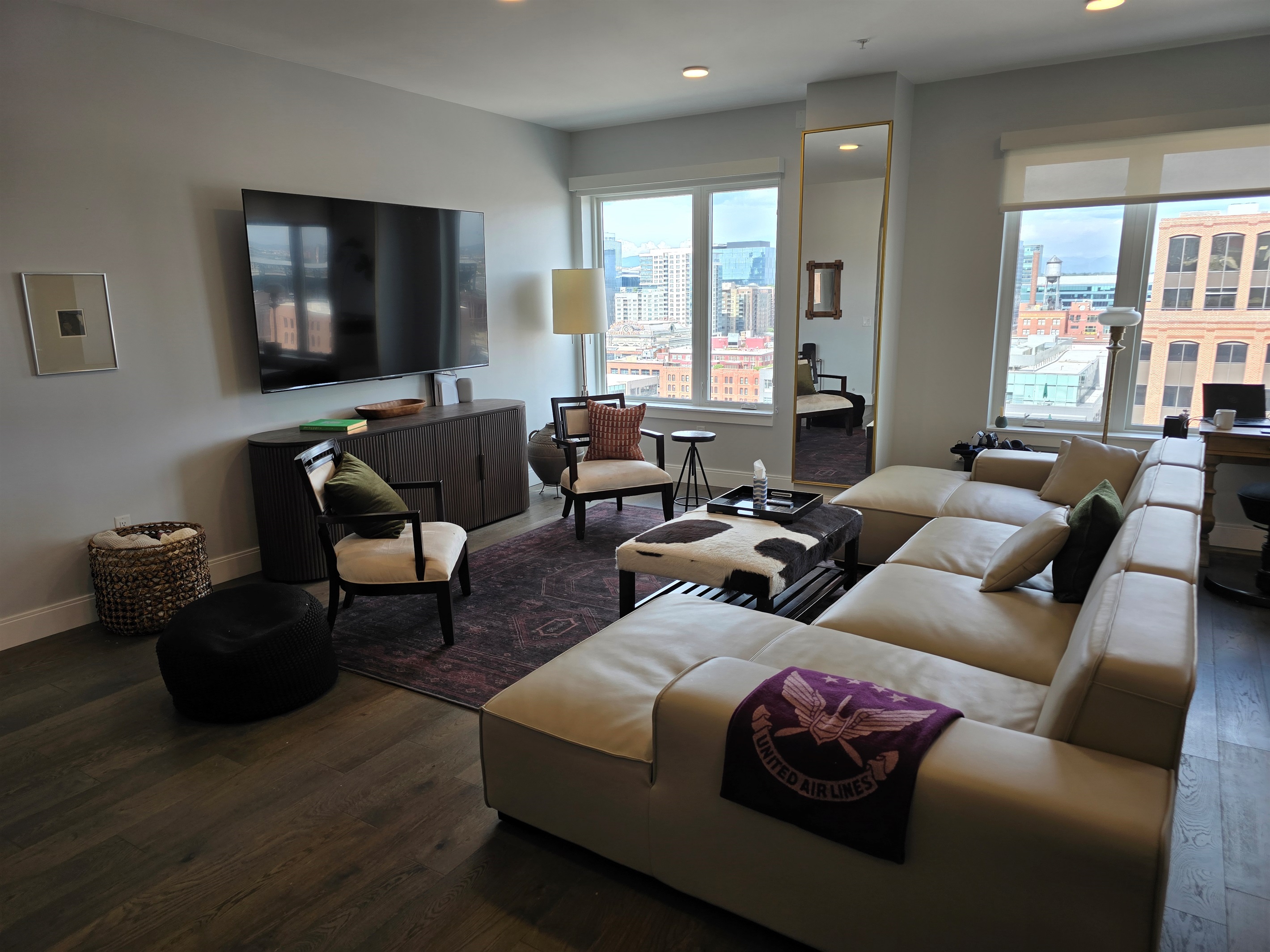 ✨ Spacious living room with designer sectional, 85" Smart TV, and skyline views.
