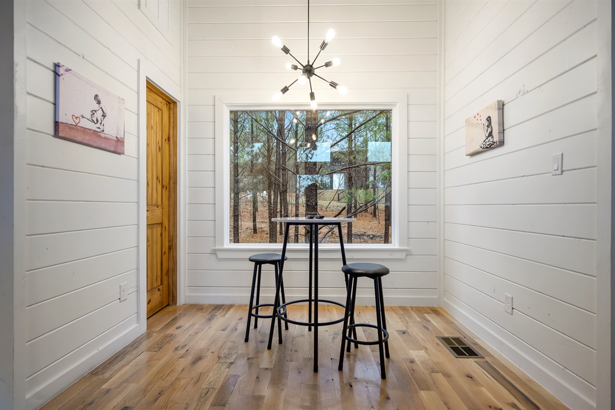 A quiet seating nook for two with a high table and chairs placed in front of a large window — the perfect spot to enjoy morning coffee while taking in the peaceful view. ☕