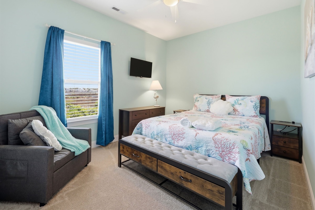 Bright queen bedroom #1 with seating, smart TV, and soft coastal tones