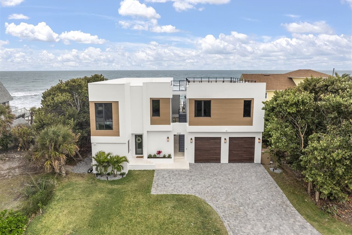 Take in the exterior view of this elegant home, featuring a welcoming door entrance, lush greenery, parking lots, sleek glass windows, and flooring. The house's vibrant color complements the stunning ocean views, offering a perfect sight-seeing spot.