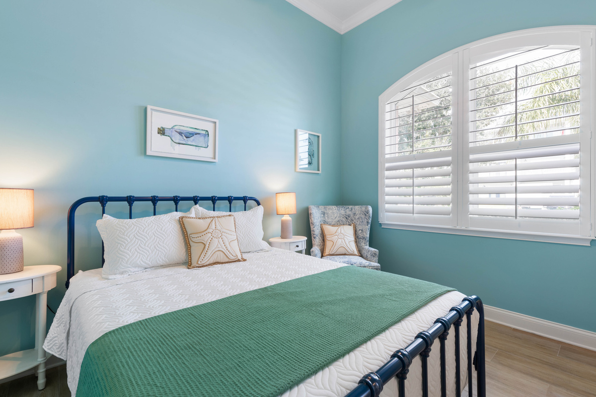 Turquoise room with a navy iron queen bed, a starfish pillow and an armchair by the arched window for quiet time.
