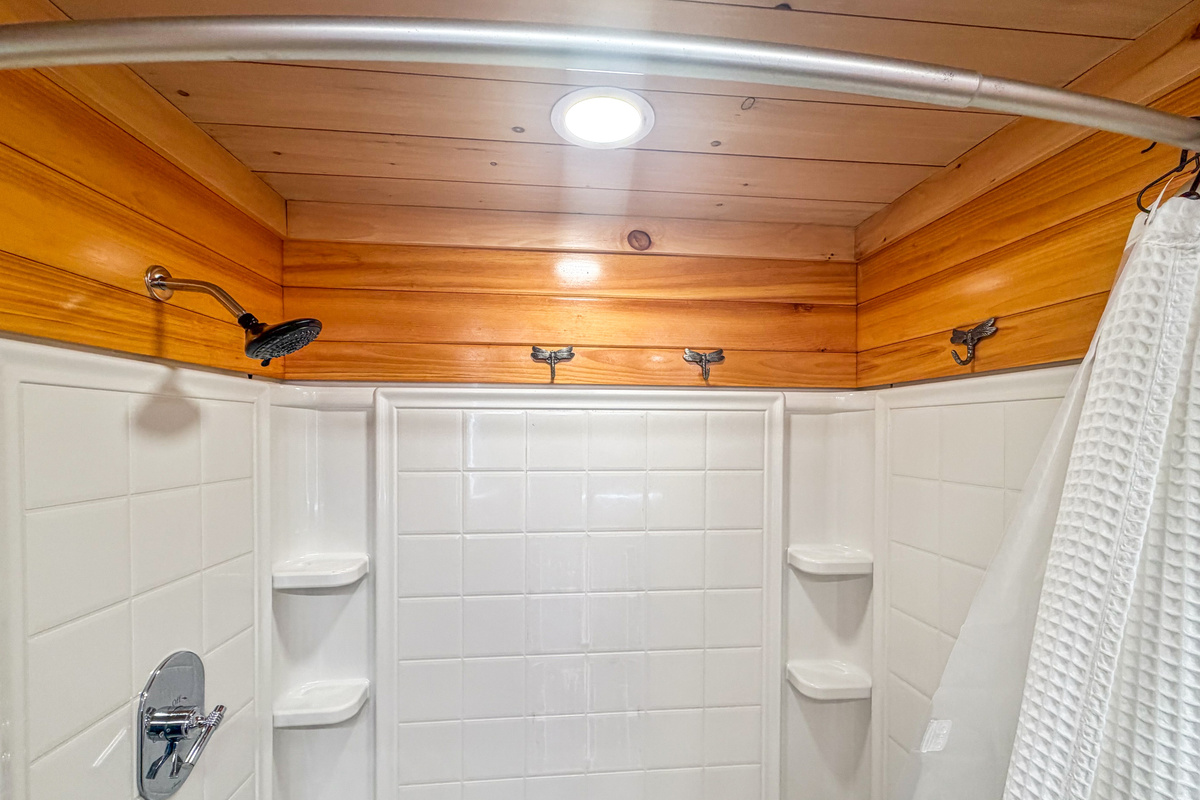 Rinse off comfortably in this pristine white surround shower enclosure. The space is equipped with multiple built-in corner shelves for soaps, decorative dragonfly wall hooks for hanging wet towels, and a dedicated ceiling canned light fixture.
