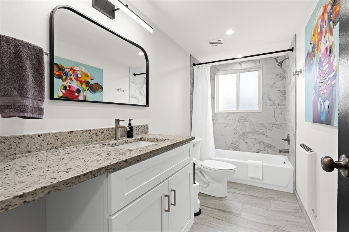 Clean and modern bathroom with full-size tub, granite vanity, and bright lighting.