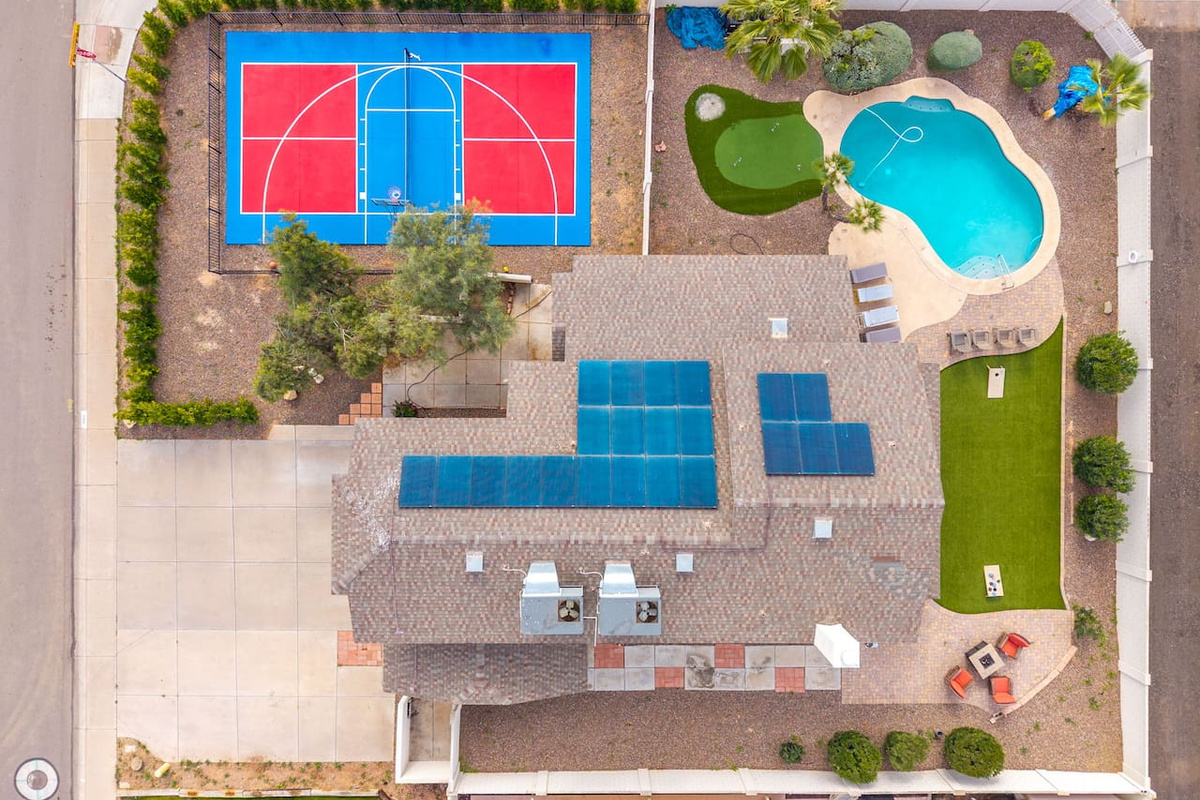 Aerial view of resort-style compound with basketball court, resort pool, solar panels, and sprawling grounds.