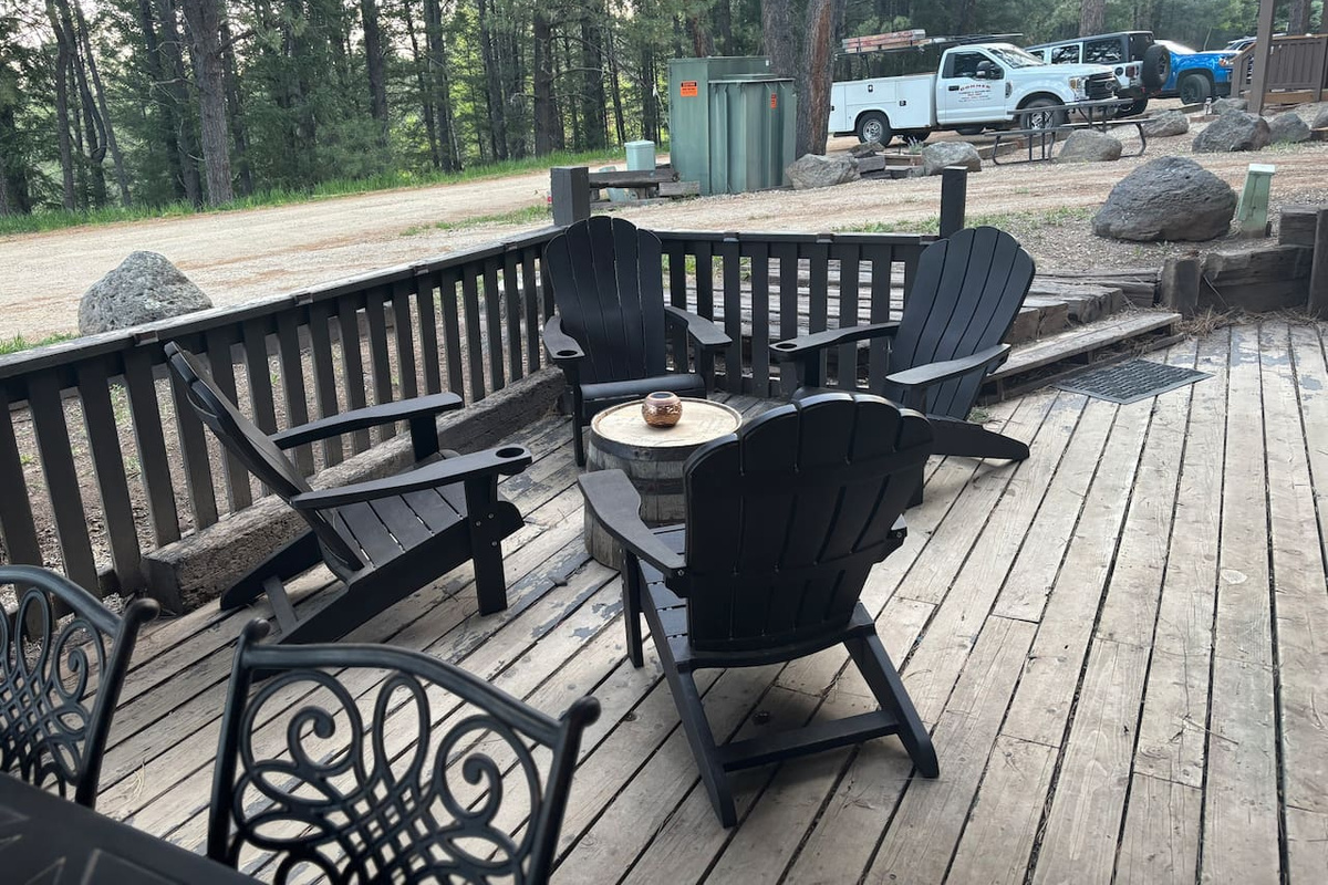 Adirondack chairs with small table in sitting are on front deck. 