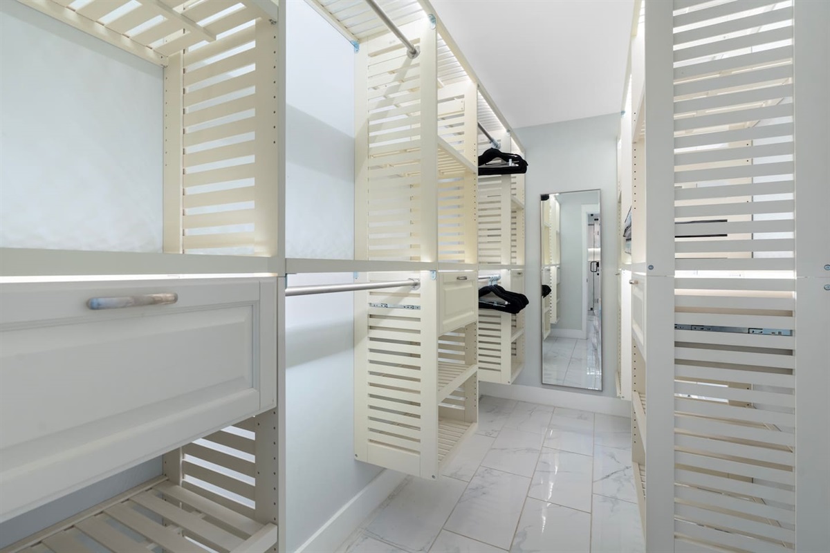 Keep everything organized with this thoughtfully designed walk-in closet featuring ample hanging space, drawers, and a full-length mirror.

